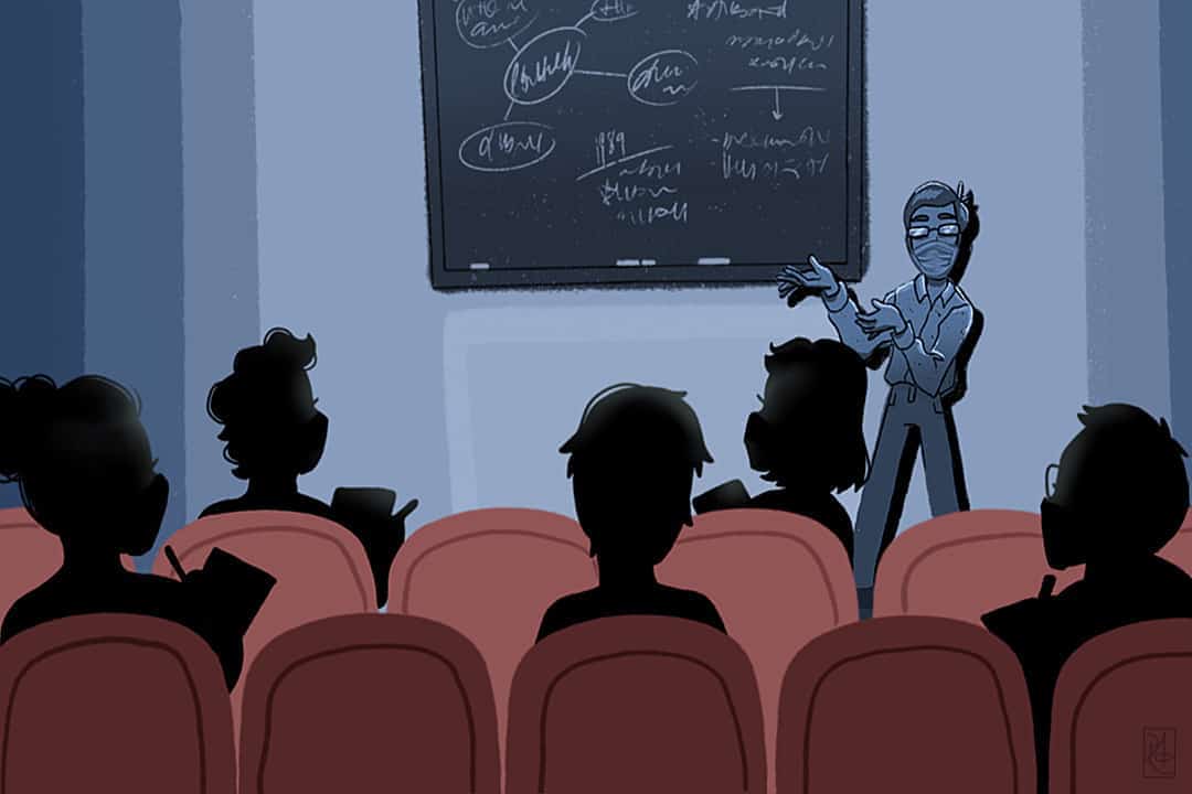 A teaching assistant in front of a blackboard speaking to students in a classroom.
