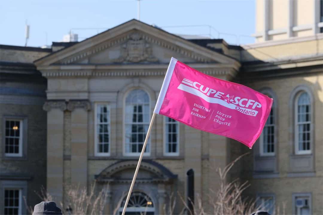 Pink CUPE flag waving in the air in front of Simcoe Hall.